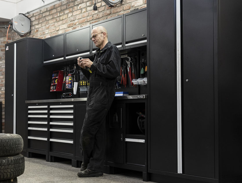 Verkstadsmiljö. Lars Edwardsson står och mekar framför en garageinredning.
